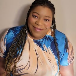 A smiling therapist from Total Life with long braided hair, wearing a colorful patterned top, photographed against a neutral indoor background.