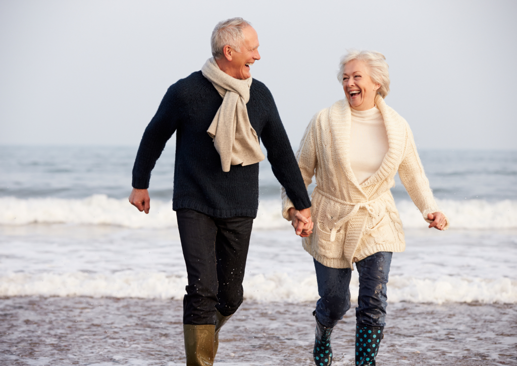 a man and woman holding hands on a beach after availing senior mental health services