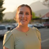 A therapist at Total Life with blonde hair styled in a braided updo, wearing a light green dress and a cross necklace. She is smiling warmly in an outdoor setting during golden hour, with mountains and a parking lot in the background. A therapist at Total Life with blonde hair styled in a braided updo, wearing a light green dress and a cross necklace. She is smiling warmly in an outdoor setting during golden hour, with mountains and a parking lot in the background. A therapist at Total Life with blonde hair styled in a braided updo, wearing a light green dress and a cross necklace. She is smiling warmly in an outdoor setting during golden hour, with mountains and a parking lot in the background.