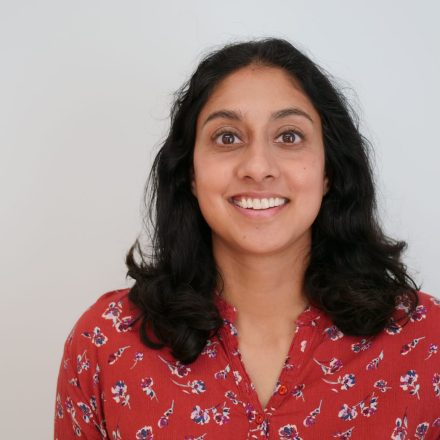 A headshot of a woman - a therapist at Total Life - with shoulder-length dark hair, wearing a red floral blouse. She is smiling warmly against a plain, light-colored background.