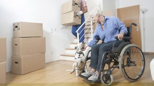 Senior in wheelchair petting dog with boxes in area