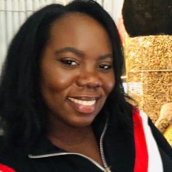 A therapist from Total Life, smiling warmly. She is wearing a zippered top with red and white accents, with a natural and cozy backdrop including soft lighting and hay, creating an inviting atmosphere.