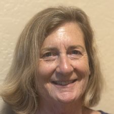 A therapist from Total Life, with shoulder-length light brown hair, smiling warmly in front of a neutral beige wall, creating a welcoming and approachable atmosphere.