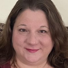 A therapist from Total Life with medium-length brown hair, a warm smile, and a magenta top, seated in a comfortable setting with a neutral background.