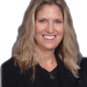 A smiling therapist from Total Life with long blonde hair, wearing a black outfit and a cross necklace, photographed against a plain white background.