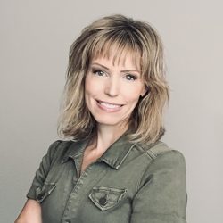 A therapist at Total Life, a professional-looking woman with shoulder-length blonde hair and bangs, smiling warmly. She is wearing a collared olive green button-up shirt and standing in front of a plain, neutral background.