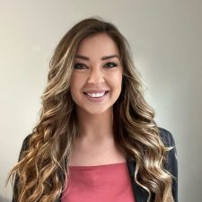 A therapist from Total Life with long wavy blonde hair, wearing a pink blouse and a black blazer, smiling in front of a neutral background.