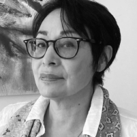 A therapist from Total Life in a black-and-white portrait. She is wearing glasses, a patterned scarf, and a white top, exuding a professional and thoughtful demeanor. The abstract artwork in the background complements her poised expression.