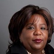 A therapist from Total Life with short dark hair, wearing a black jacket and pearl necklace, posing against a gray background.