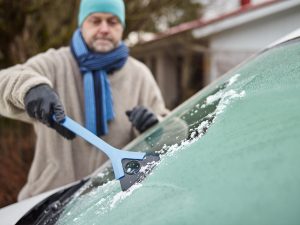 man cleans a frozen windshield